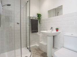 Un baño moderno con ducha envuelta en vidrio, lavamanos pedestal y retrete.