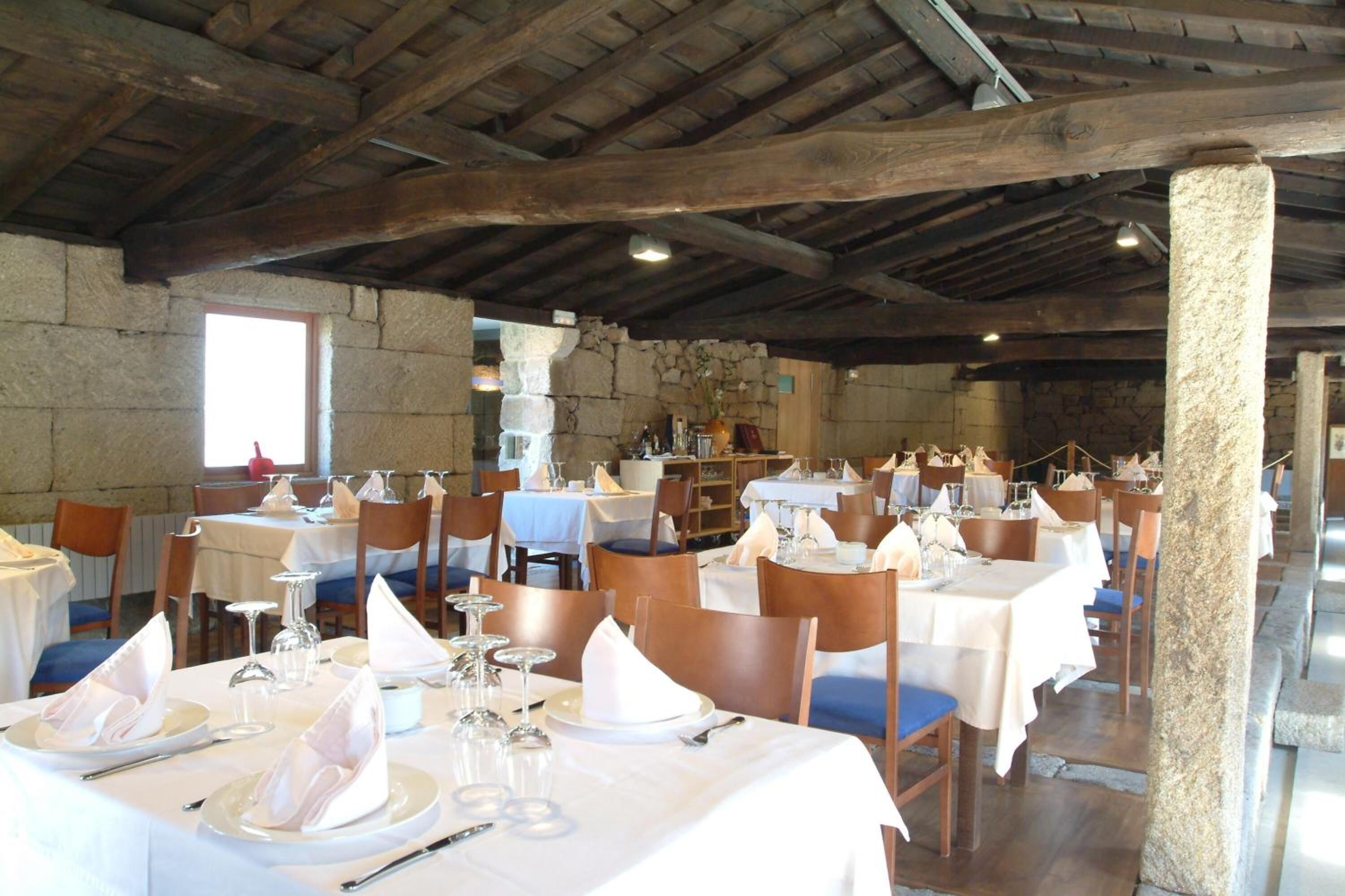 A restaurant with wooden beams, stone walls, and tables set for dining.
