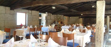 A restaurant with wooden beams, stone walls, and tables set for dining.