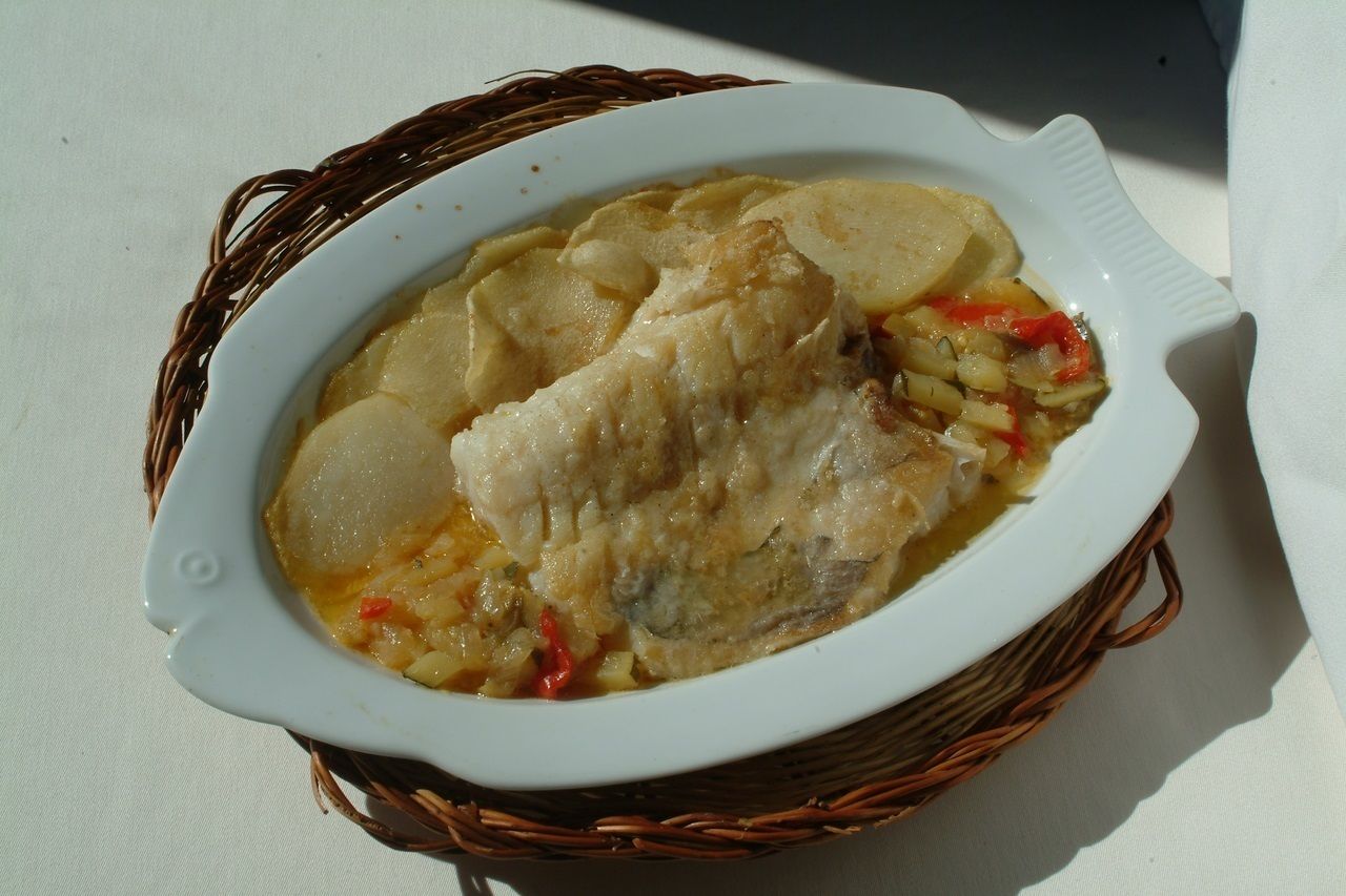 Un plat ceràmic blanc amb un peix i patates, col·locat en una cistella teixida.