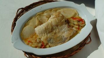 Un plat ceràmic blanc amb un peix i patates, col·locat en una cistella teixida.