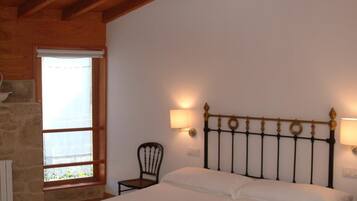 A bedroom with two beds, wooden ceiling beams, a stone wall, and a window with a view.