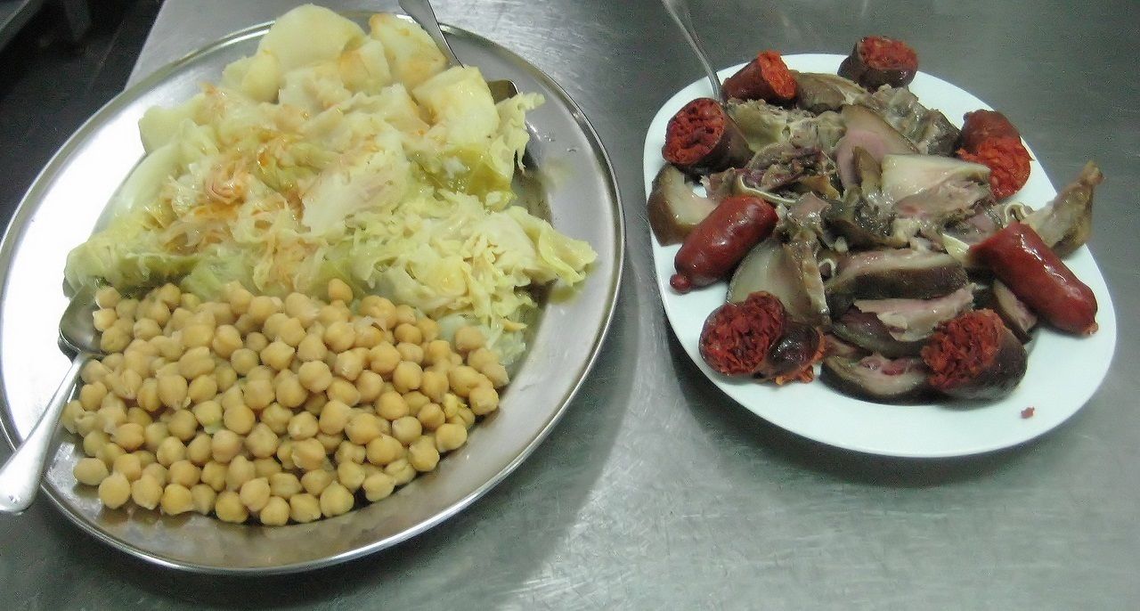 Dos platos de comida, uno con papas, repollo y garbanzos, y el otro con salchichas y carne.