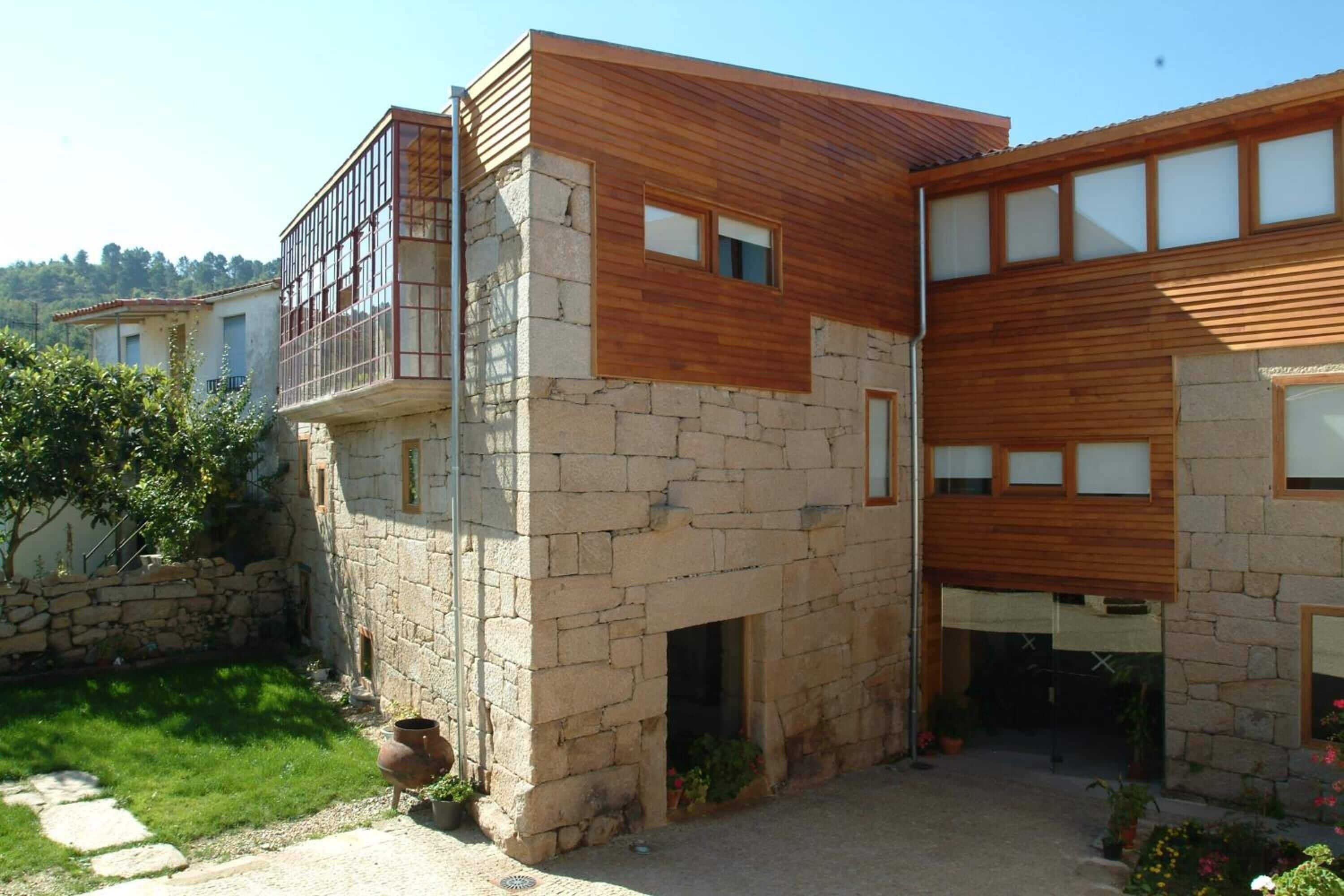 Une maison moderne à deux étages, dotée d’une façade en pierre et d’étages supérieurs en bois.