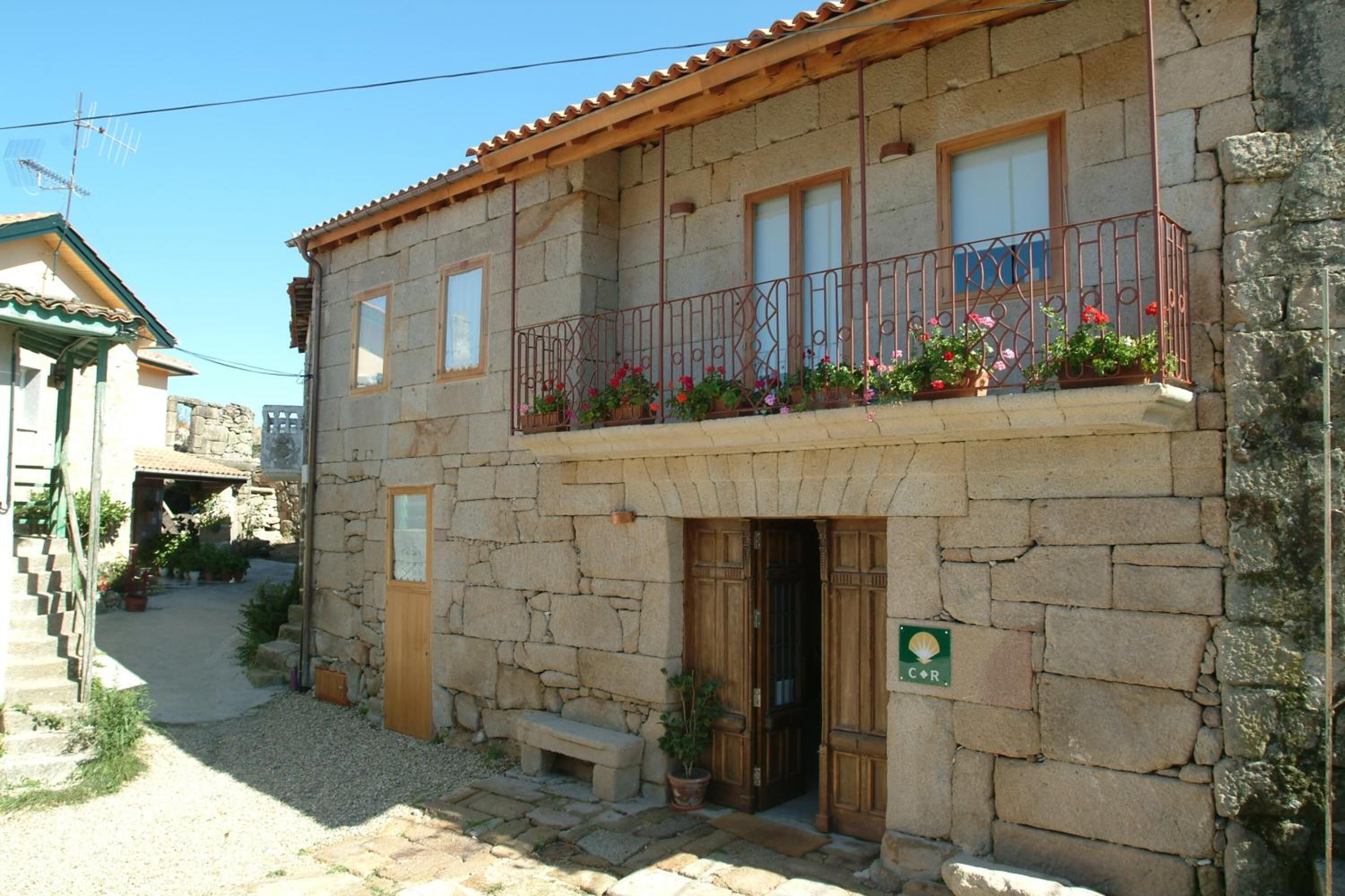 A stone building with a wooden balcony, a door, and a small garden area.