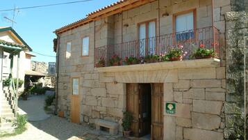A stone building with a wooden balcony, a door, and a small garden area.