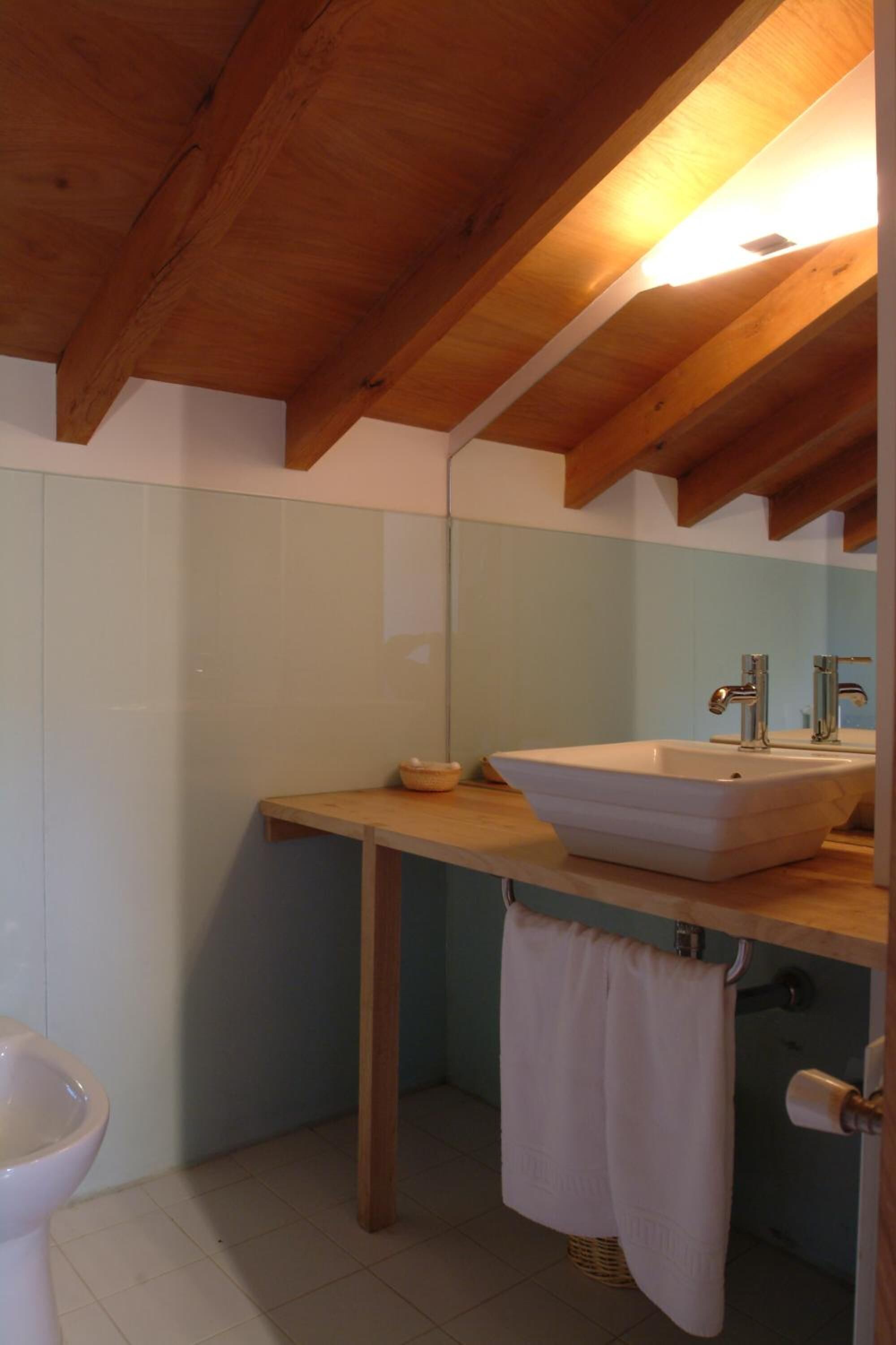 A bathroom with a wooden ceiling, a white sink, a mirror, and a toilet.