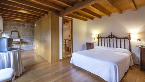 Un dormitorio con techo de madera, una cama con ropa de cama blanca, una mesita de noche y un escritorio con una silla.