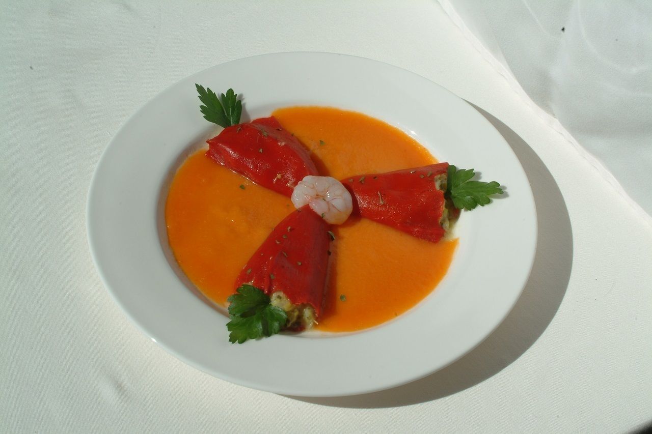 Un plato blanco con un guiso de tomates rellenos y camarones sobre un mantel blanco.