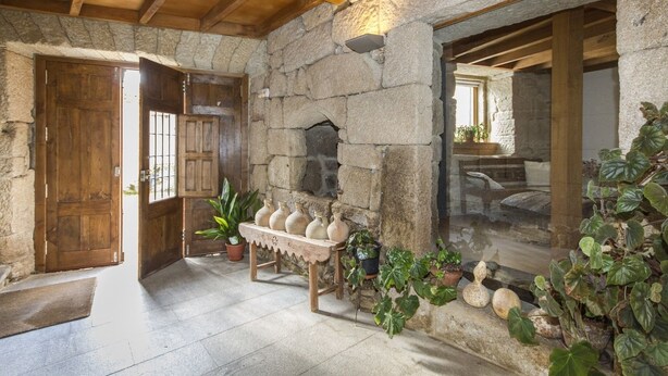 Interior rústico de piedra con una puerta de madera, un muro de piedra y un banco con plantas en macetas.