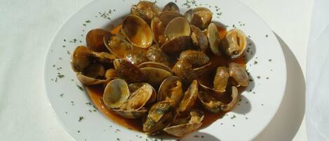 Une assiette de palourdes servies dans une sauce à base de tomates, garnies d’herbes aromatiques.