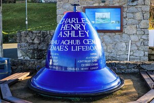 Un monumento azul con inscripciones, un muro de piedra y una placa en el fondo.