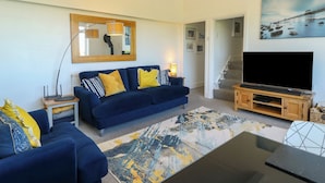 A living room with a sofa, a TV, a painting, and a staircase. - Little Orme View (Llandudno)