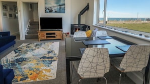 A living room with a TV, fireplace, dining area, and a view of the beach. - Little Orme View (Llandudno)