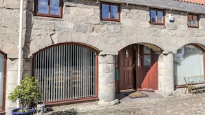 A stone building with a tiled roof, large arched windows, and a wooden door. - The Mistal (Alnwick)
