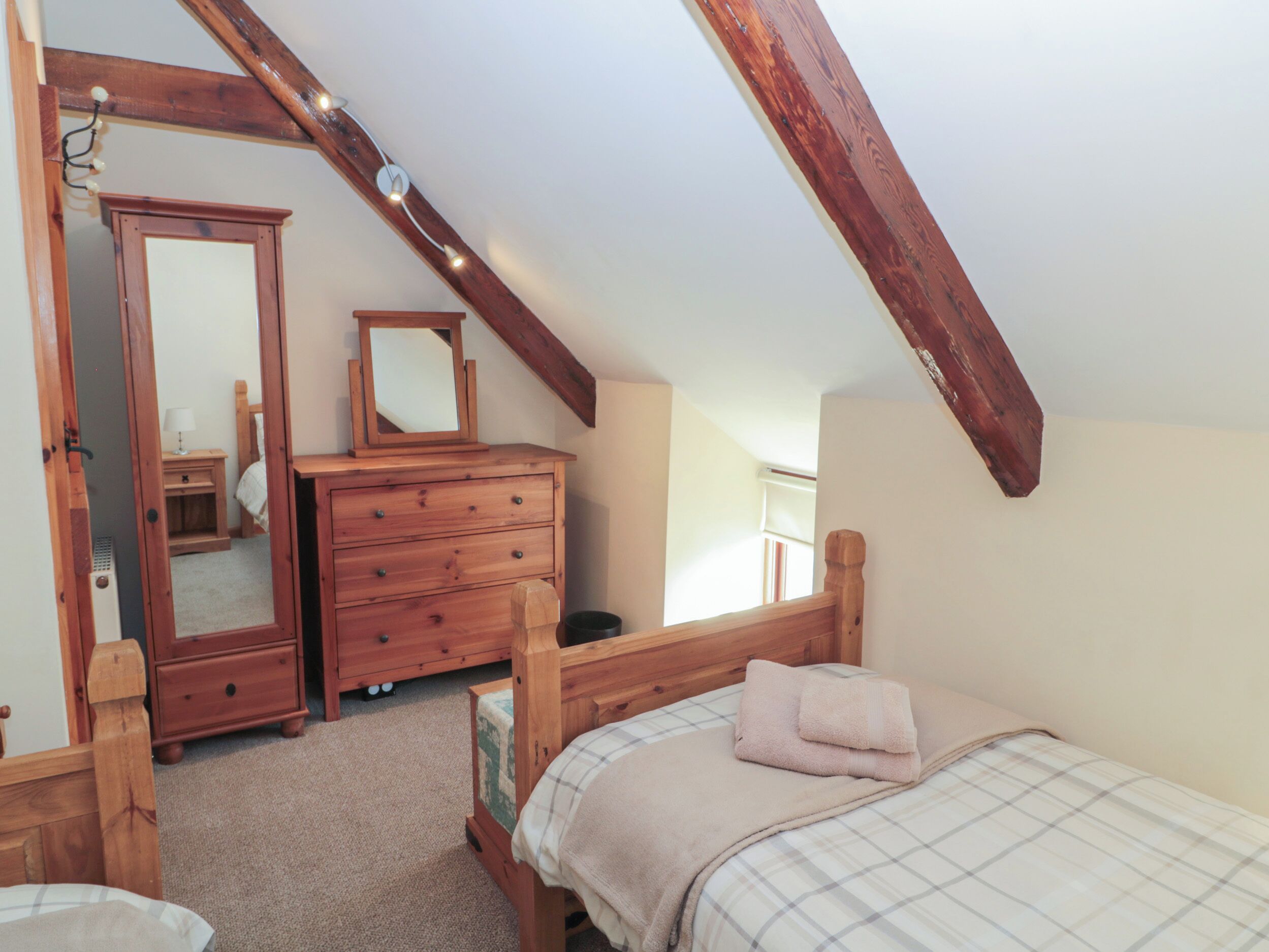 A bedroom with a wooden bed, a dresser, a mirror, and a sloped ceiling with exposed beams.
