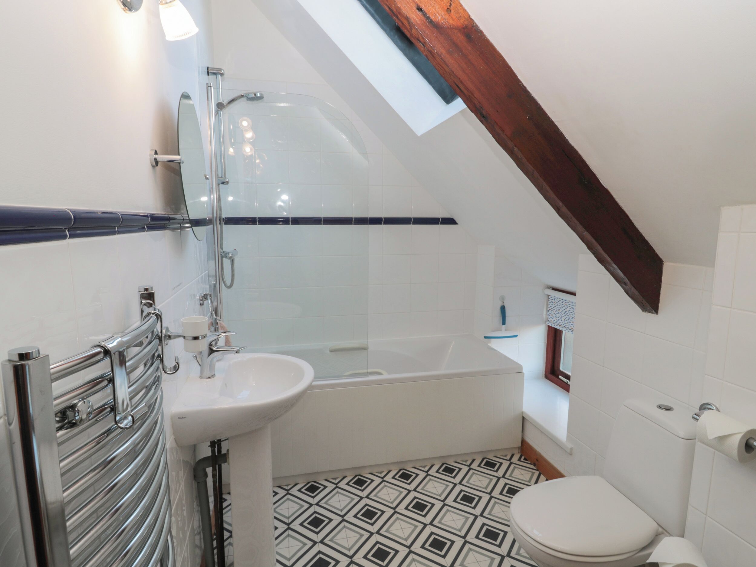 A bathroom with a shower, sink, and toilet, featuring a geometric tile floor and a skylight.