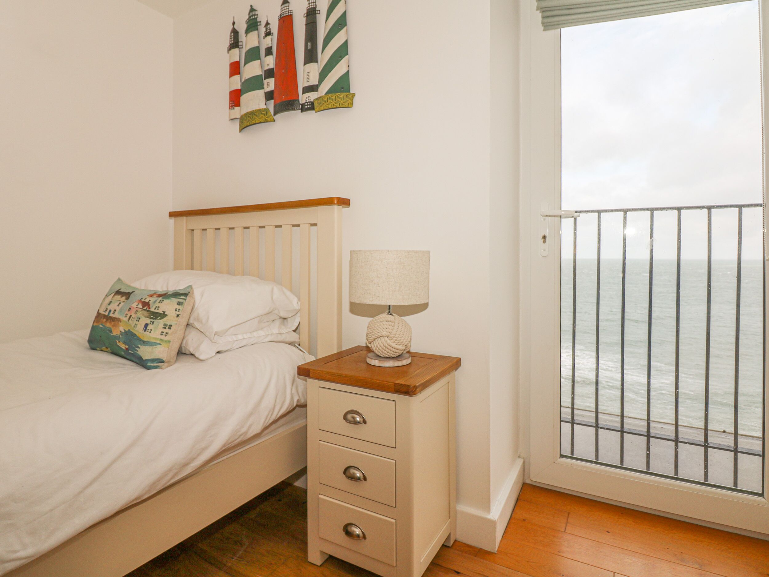 A bedroom with a bed, bedside table, lamp, and a view of the sea through a balcony door.