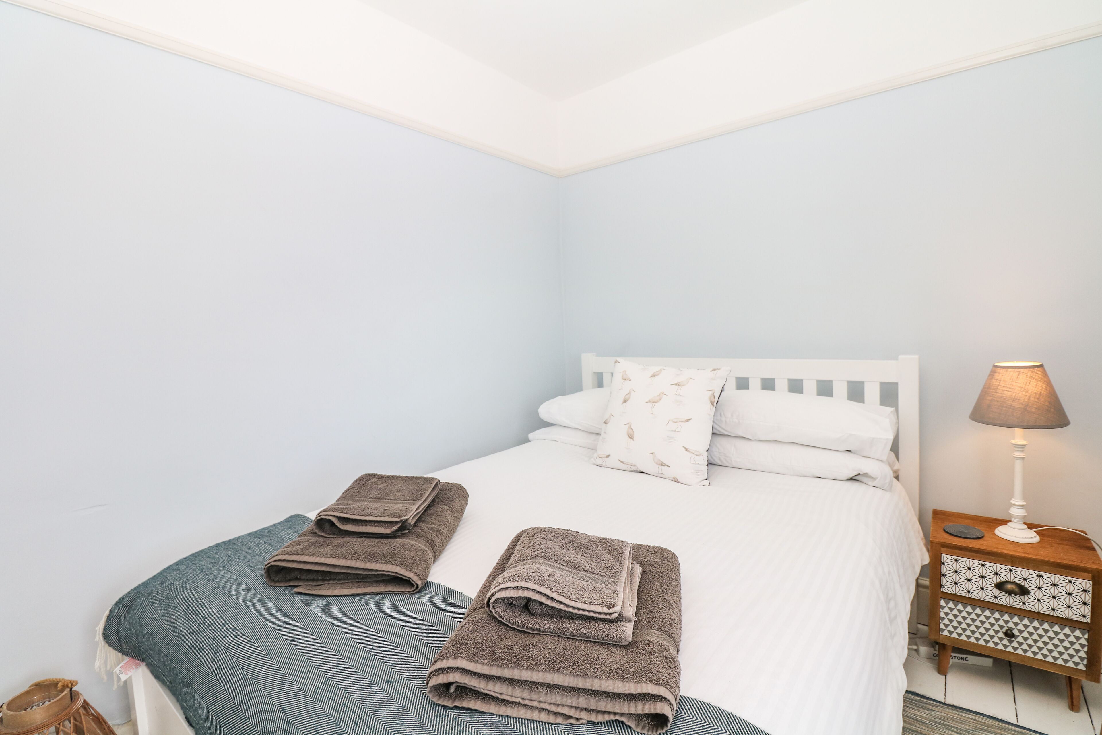 A neatly made bed with folded towels, a bedside lamp, and a patterned rug.