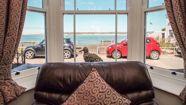 A room with a view of the sea, a brown leather sofa, and patterned curtains. - The Crab Shell (Bideford)