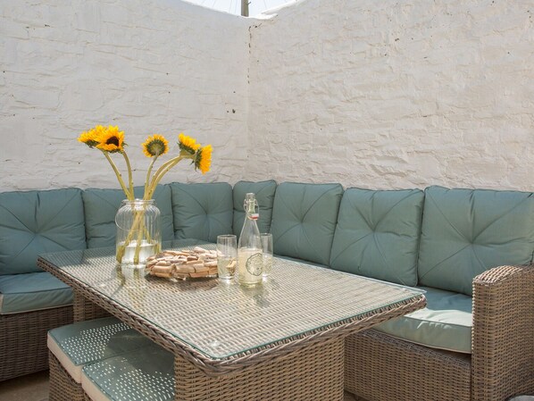 A wicker table with a glass top, surrounded by green cushioned seating. - The Crab Shell (Bideford)