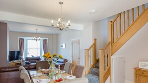 A dining area with a wooden table set for four, a chandelier, and a staircase leading to an upper floor. - The Crab Shell (Bideford)