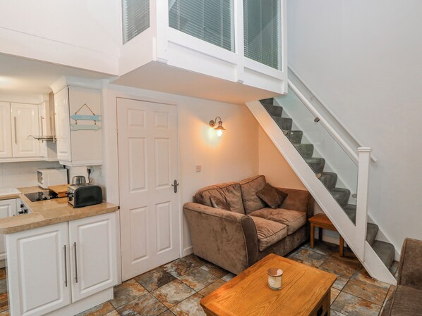 A compact living space with a kitchenette, a sofa, a small table, and a staircase.