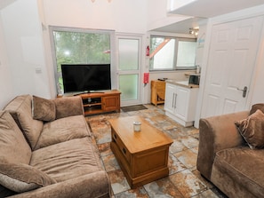 A living room with a TV, two sofas, a coffee table, and a kitchen area with cabinets and a door.