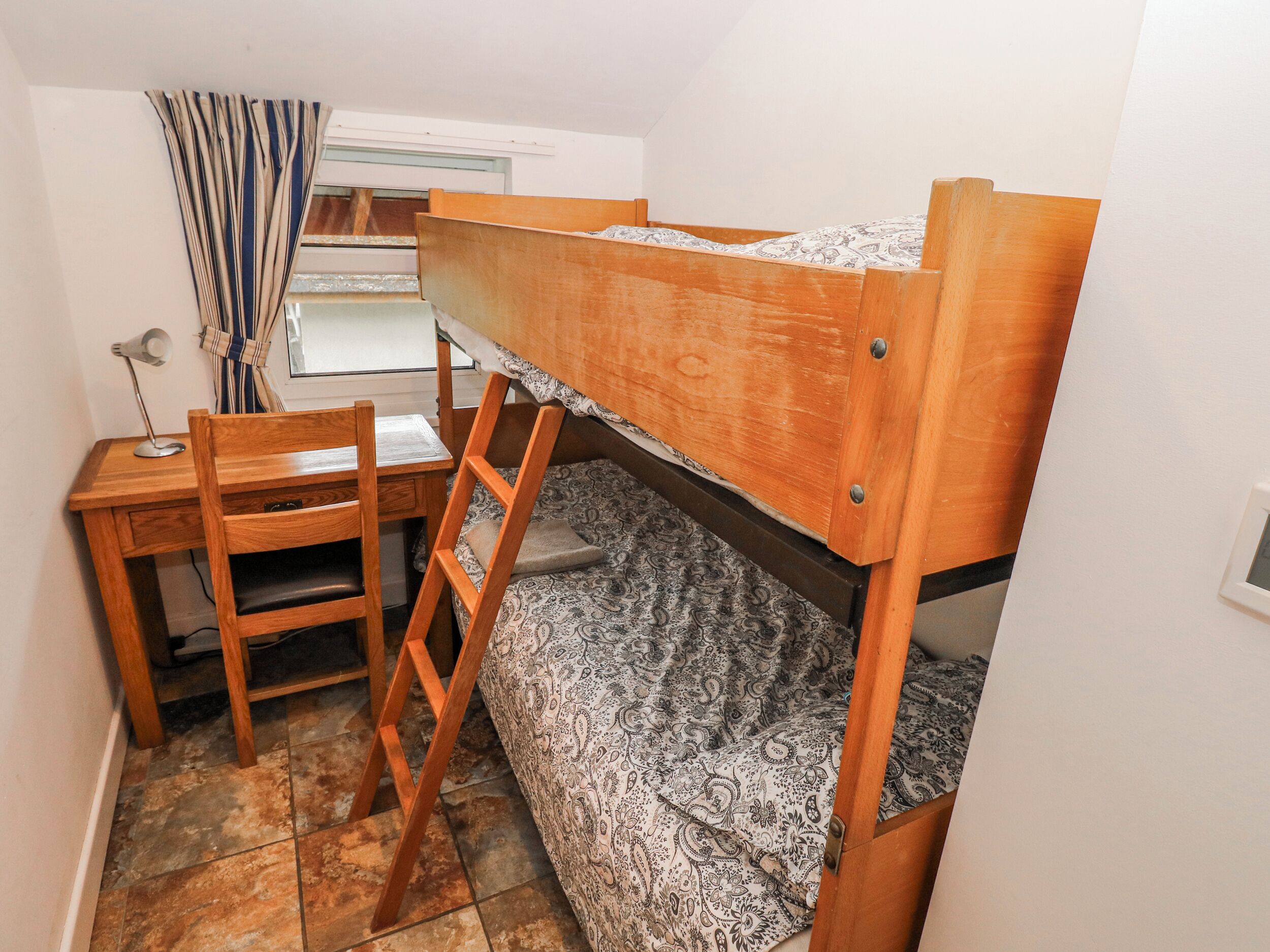 Un letto a castello con scrivania, sedia e una coperta decorata.