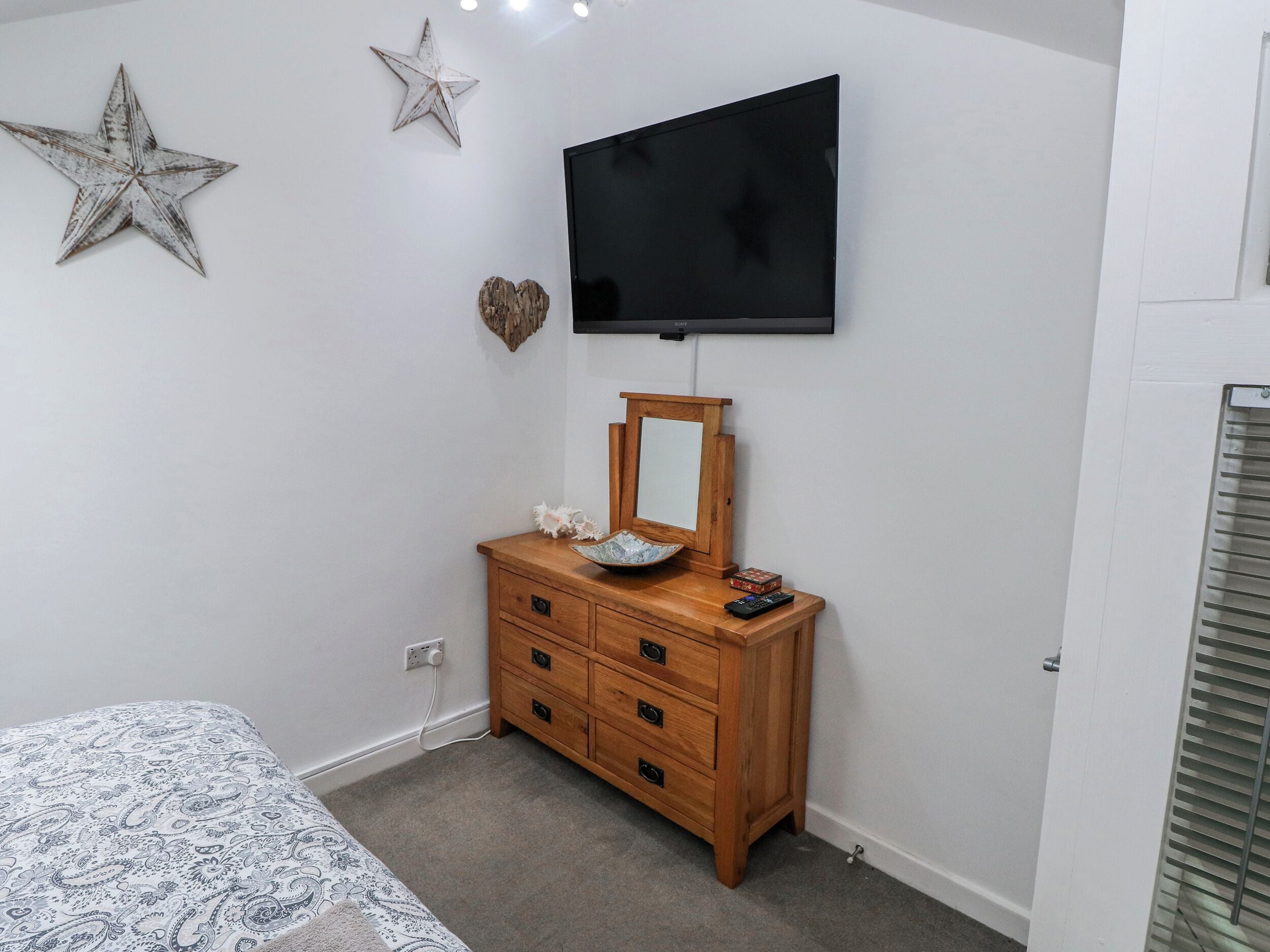 Un dormitorio con cama, cómoda, televisor y decoración de estrellas y corazones en la pared.