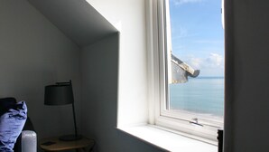 A room with a window overlooking a body of water, a lamp, and a chair. - The Eaves (Folkestone)