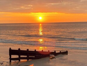 A beach scene with a wooden bench and the sun setting over the ocean. - The Cartwheel (Narberth)