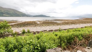 Un paisaje costero con playa, vegetación y montañas a lo lejos.