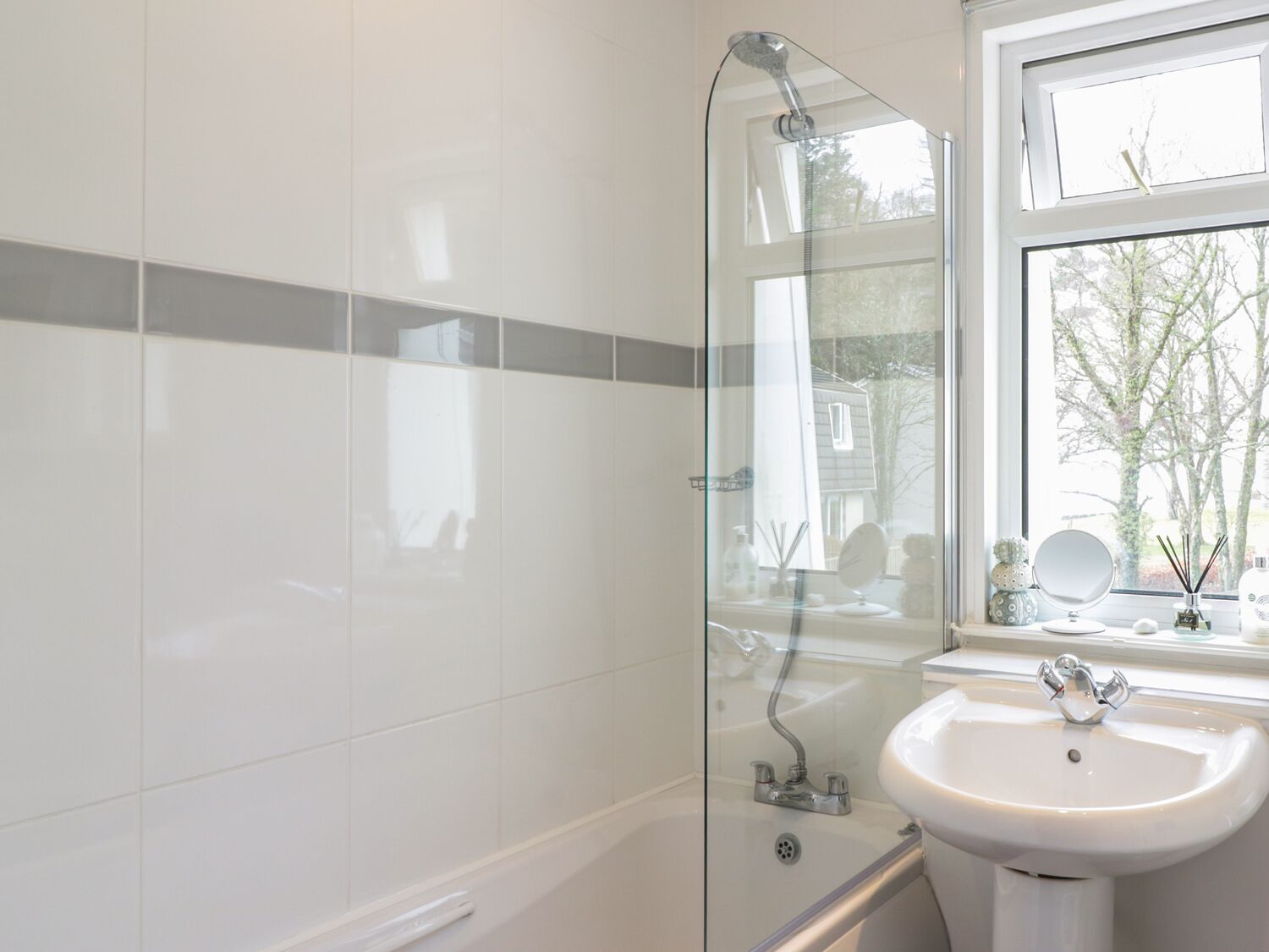 A modern bathroom with a glass shower enclosure, a white sink, and a window offering a view of the outdoors.