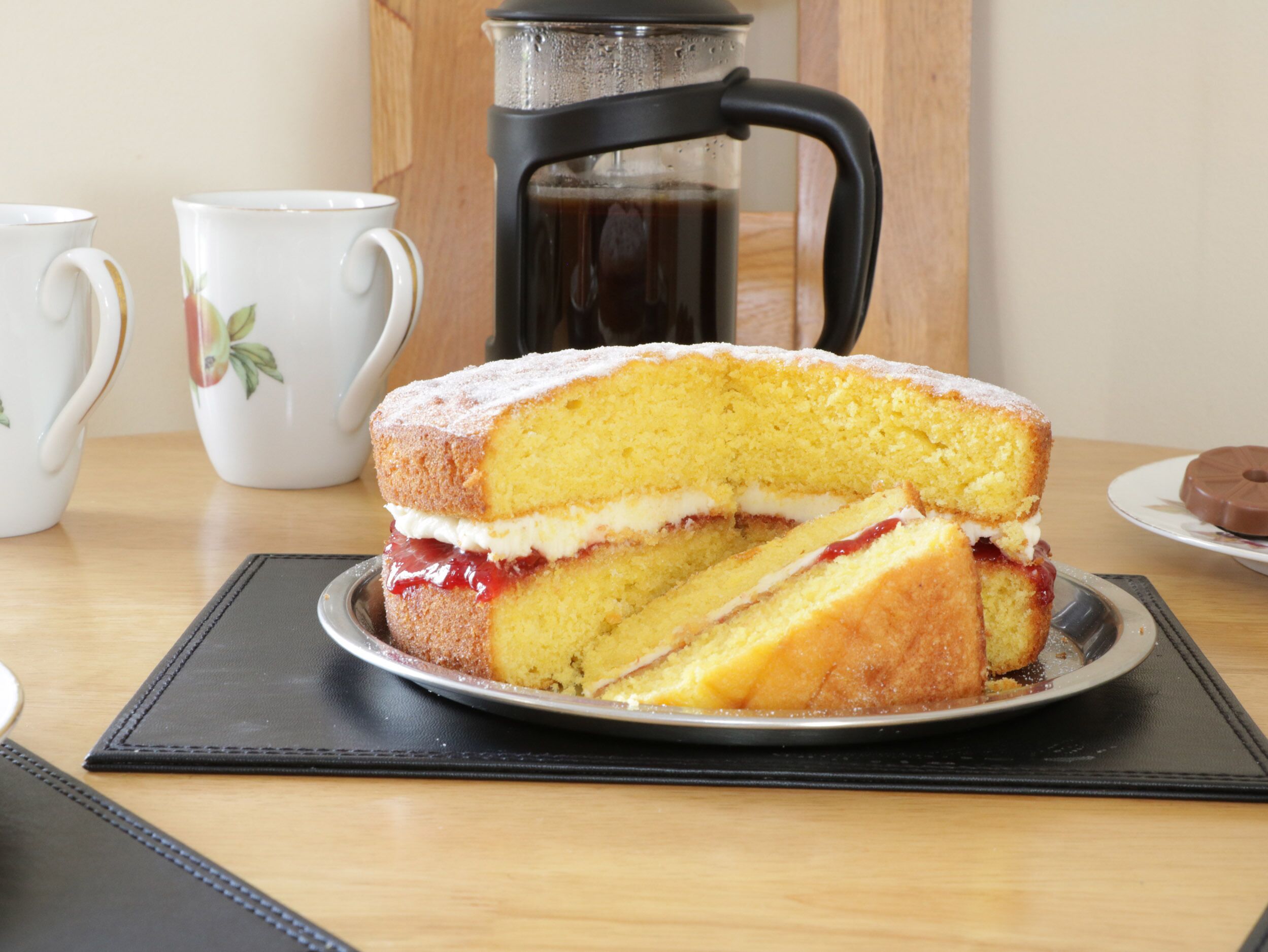 A slice of sponge cake with jam and cream on a plate.