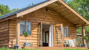 A wooden cabin with a porch, large windows, and a small garden area with plants and outdoor furniture. - Stoney-brook Lodge (Ludlow)