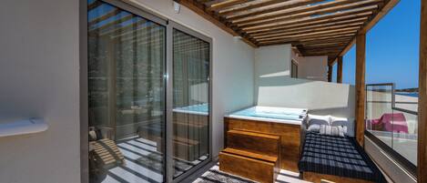 A balcony with a wooden pergola, a glass door leading to a seating area, and a small bed with a blue bedspread.