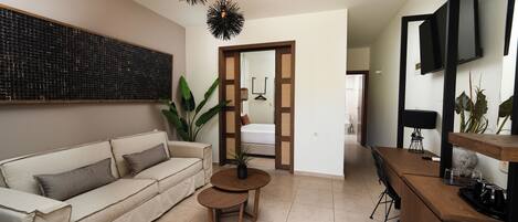 A modern living room with a sofa, a small round table, a TV mounted on the wall, and a wooden bar counter.