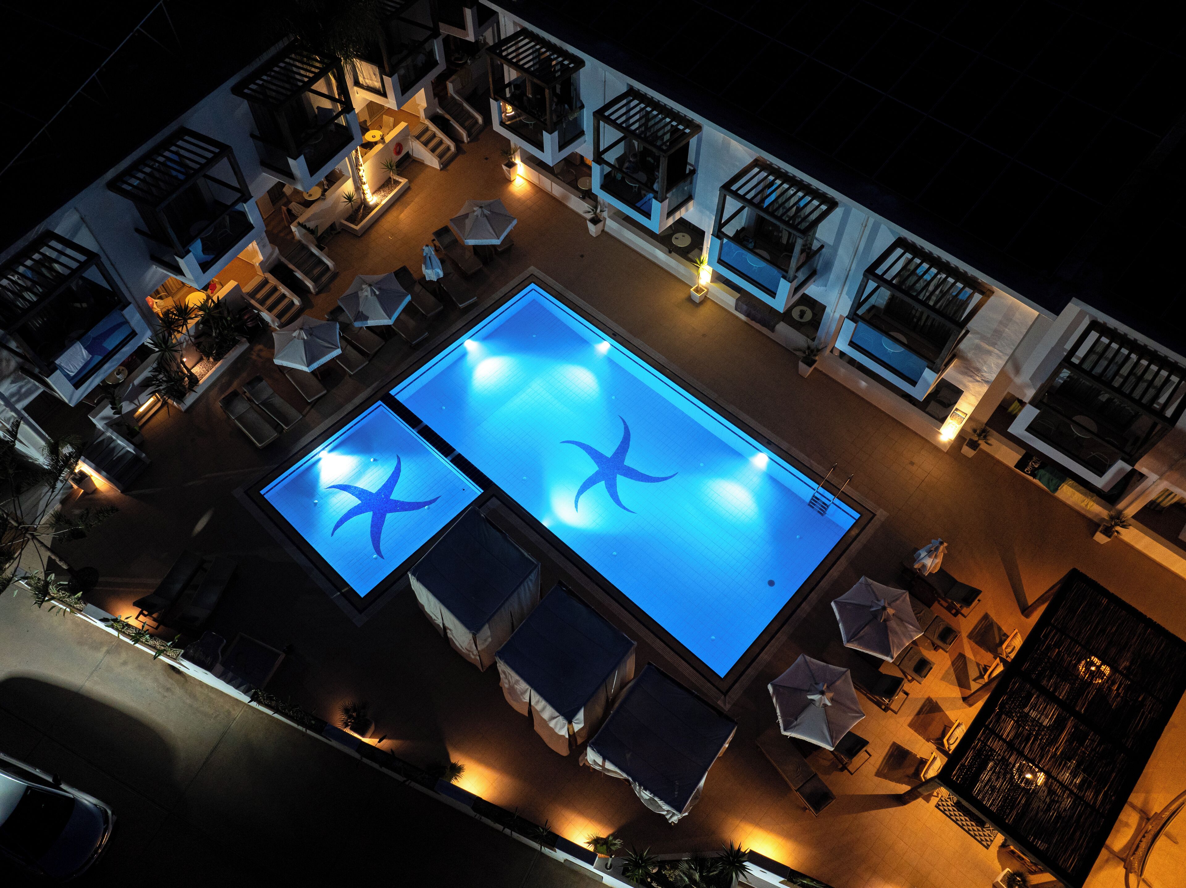 An aerial view of a rooftop pool area with two swimming pools, lounge chairs, and umbrellas.