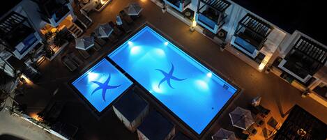 An aerial view of a rooftop pool area with two swimming pools, lounge chairs, and umbrellas.