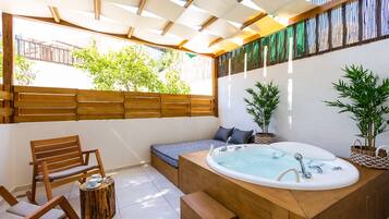 A spa area with a wooden bench, a small round table with a cup and saucer, and a large bathtub.