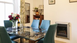 Un coin repas avec une table en verre, des chaises bleues, un vase de fleurs, une bouteille et une cheminée.
