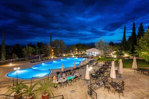 Une piscine entourée d’un espace patio avec des tables et des chaises, ainsi que de transats et de parasols.