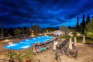 Una piscina con sillones y sombrillas, rodeada por un patio con mesas y sillas.