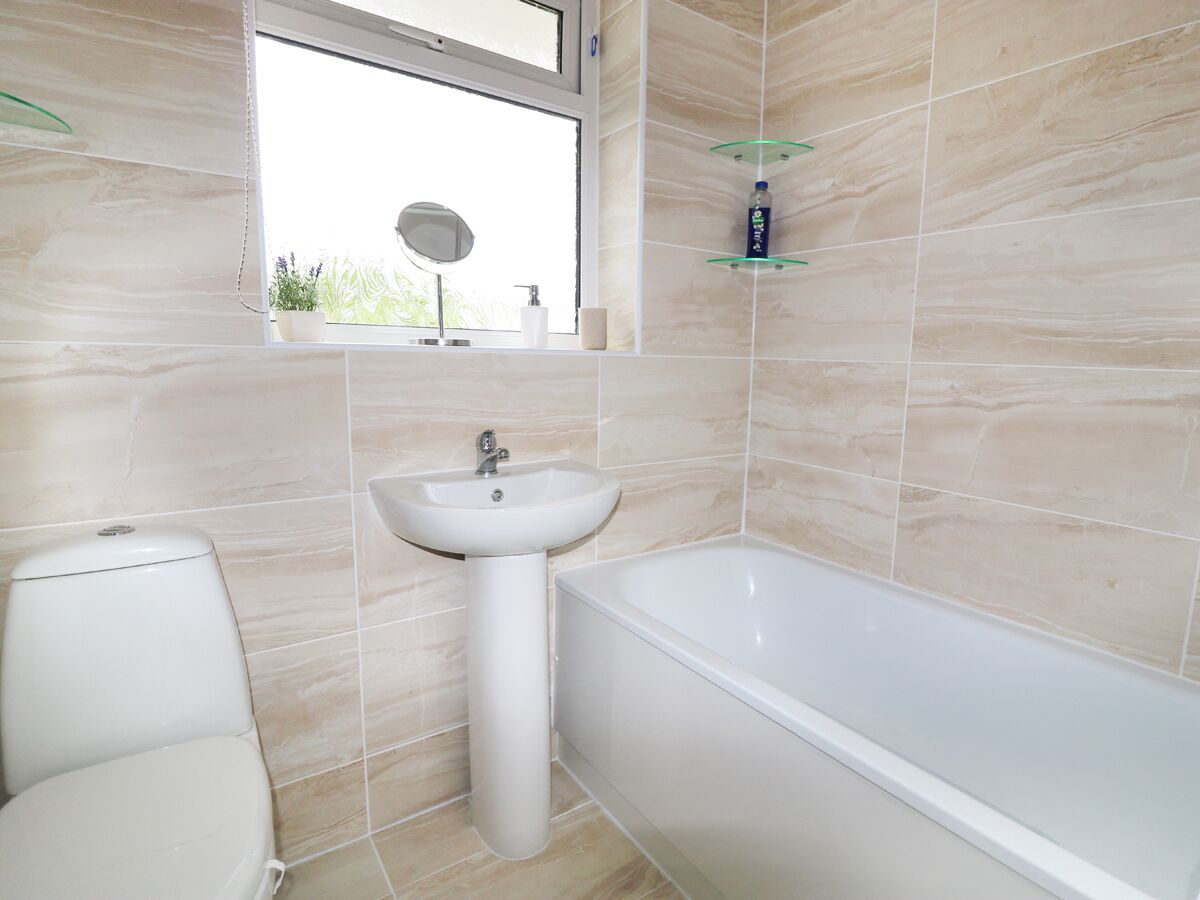 A bathroom with a toilet, sink, and bathtub. There is a window above the sink and a mirror on the wall.