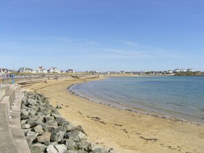 Una playa arenosa con un rompeolas rocoso y casas al fondo.