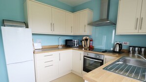 A kitchen with white cabinets, a refrigerator, an oven, a microwave, and a sink. - Anneddle (Holyhead)