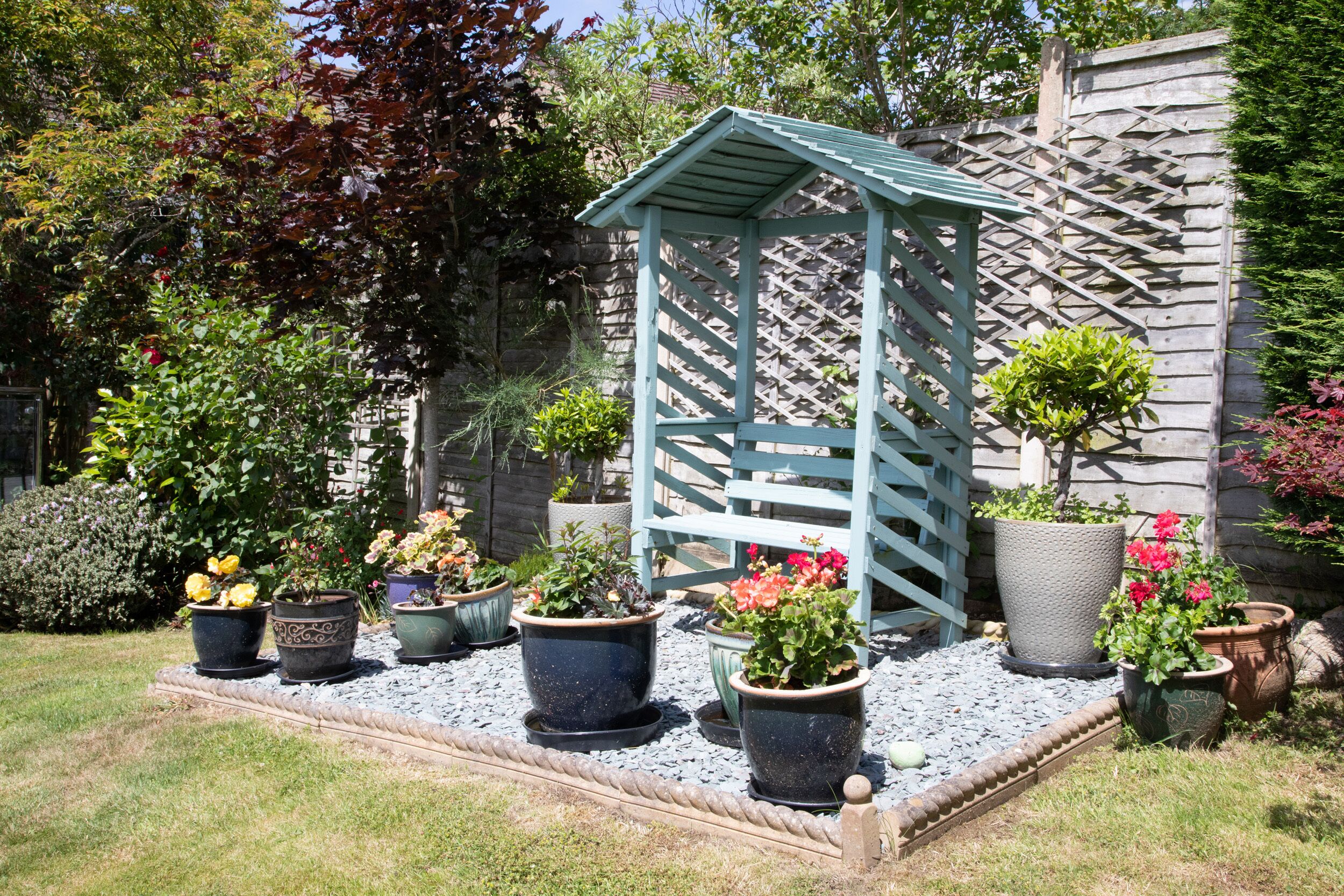 Ein Garten mit einer Holz-Pergola, verschiedenen Blumentöpfen und einer Steinmauer.