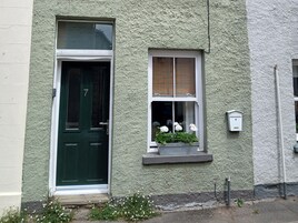 Un edificio de dos pisos con una puerta verde y una ventana con un balcón de flores.