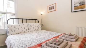 Un dormitorio con cama, almohadas, una lámpara de noche, un cuadro enmarcado y una ventana.